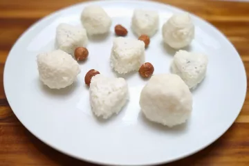 Keto coconut fat bombs in round and heart shapes on a white plate with hazelnuts.