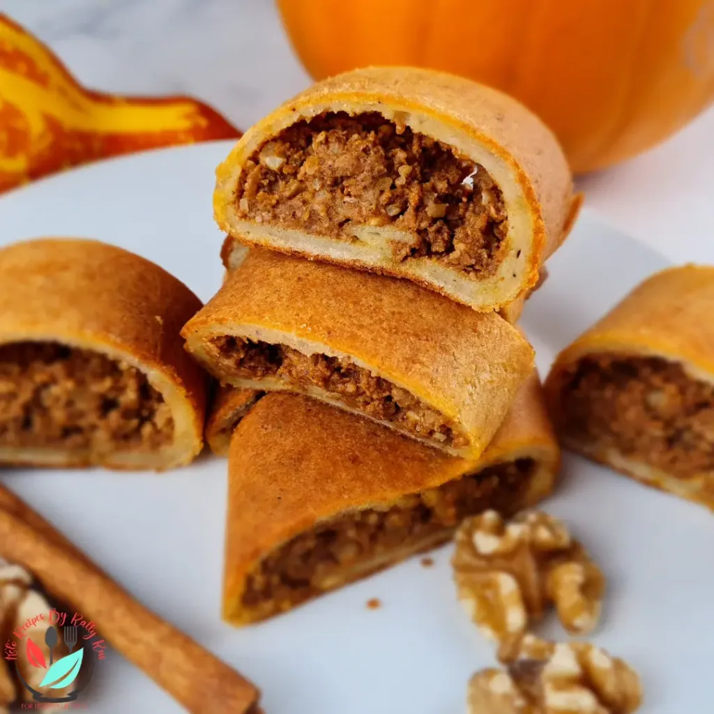 A plate of keto pumpkin pinwheels (keto tikvenik) with walnuts and cinnamon sticks on a white plate