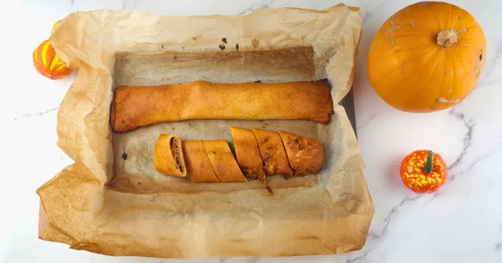 A plate of keto pumpkin pinwheels (keto tikvenik) with walnuts and cinnamon sticks on a white plate