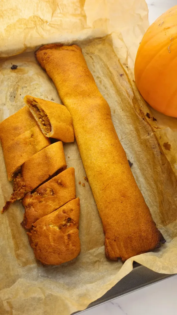 A plate of keto pumpkin pinwheels (keto tikvenik) with walnuts and cinnamon sticks on a white plate