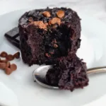 A keto gluten free chocolate brownie mug cake on a white plate with chocolate chunks and chocolate chips on top.