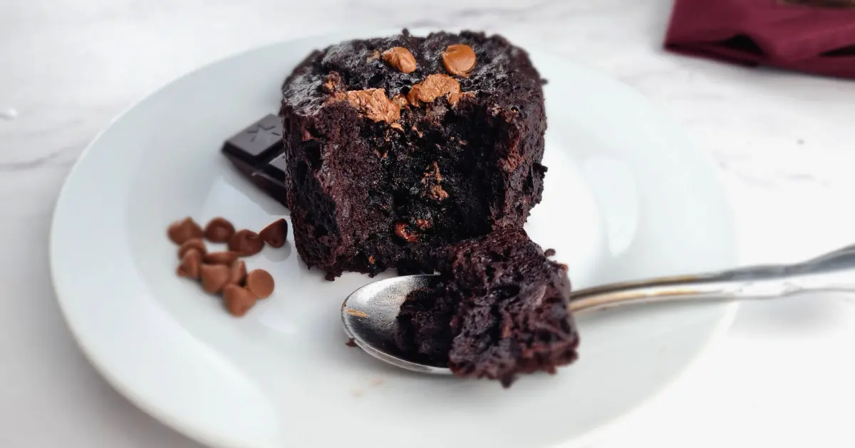 A keto gluten free chocolate brownie mug cake on a white plate with chocolate chunks and chocolate chips on top.