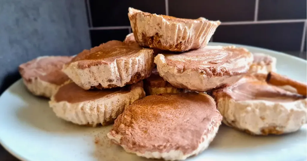 Twelve Keto Gingerbread Cheesecakes on a black plate with a cinnamon stick on the side.