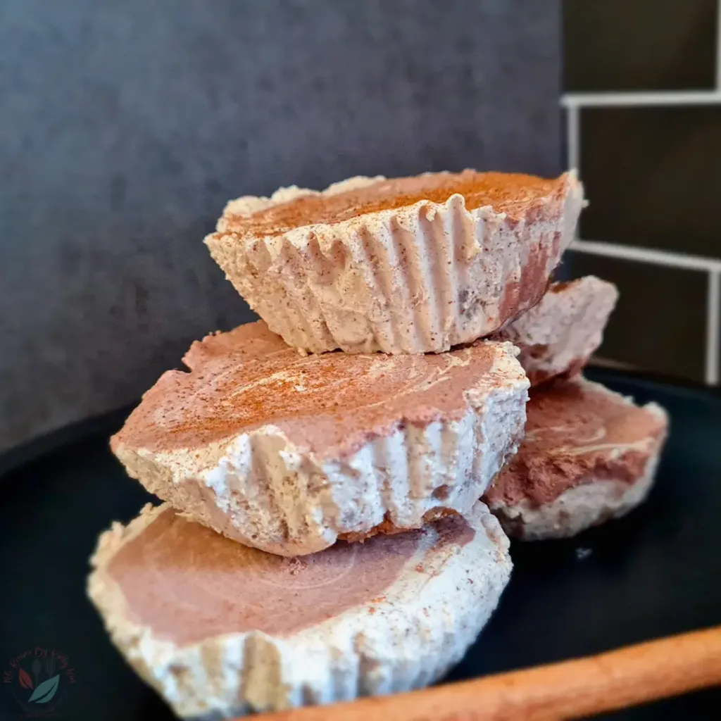 Twelve Keto Gingerbread Cheesecakes on a black plate with a cinnamon stick on the side.