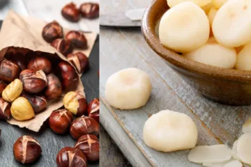 A photo of a bowl of roasted water chestnuts on a wooden table. The water chestnuts are dark brown and have been roasted until they are slightly charred. The bowl is black and has a white stripe around the rim. The table is made of dark wood and has a rustic texture.