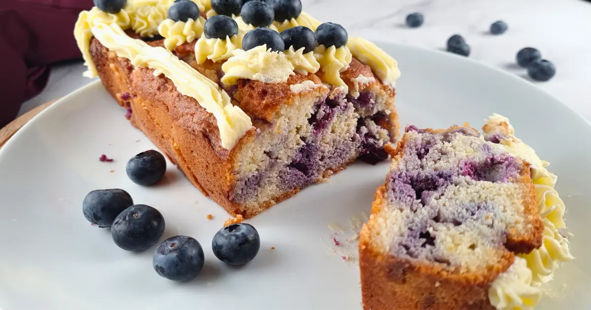A delicious keto blueberry creme fraiche pound cake topped with intricate swirls of keto Royal Icing Buttercream, presented on a white plate.