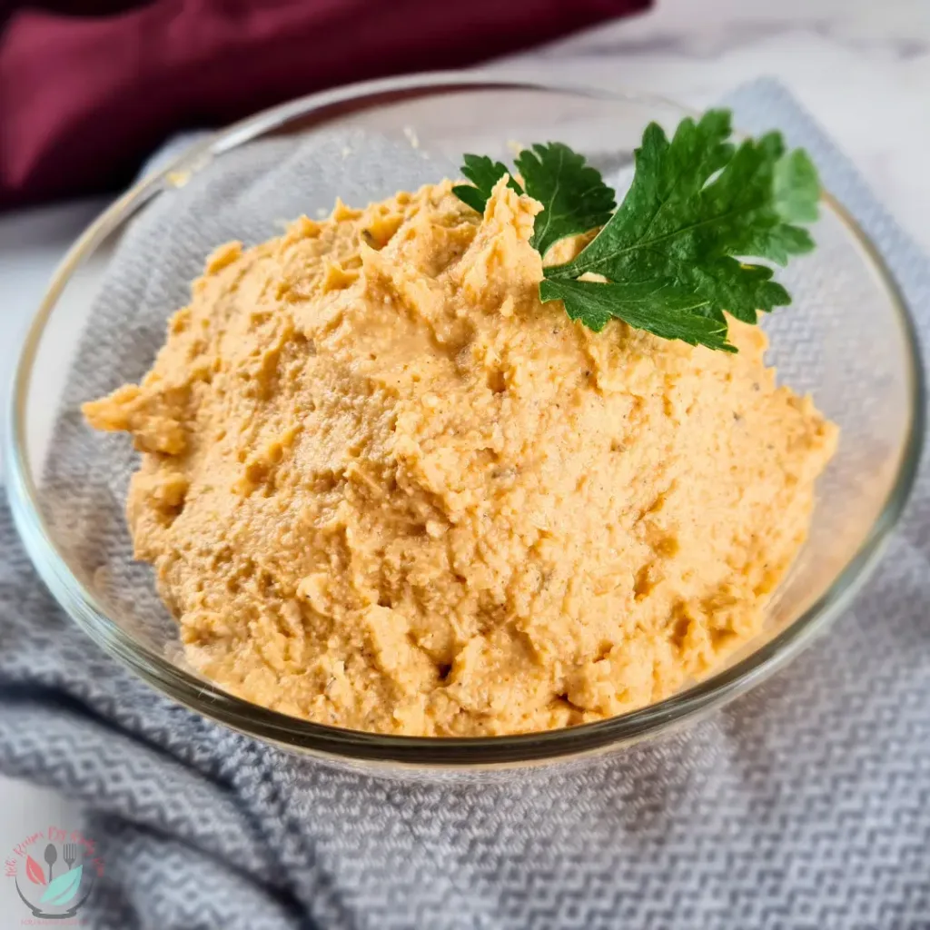 A bowl of creamy keto Cajun Alfredo sauce garnished with a fresh parsley leaf, placed on a textured grey cloth.