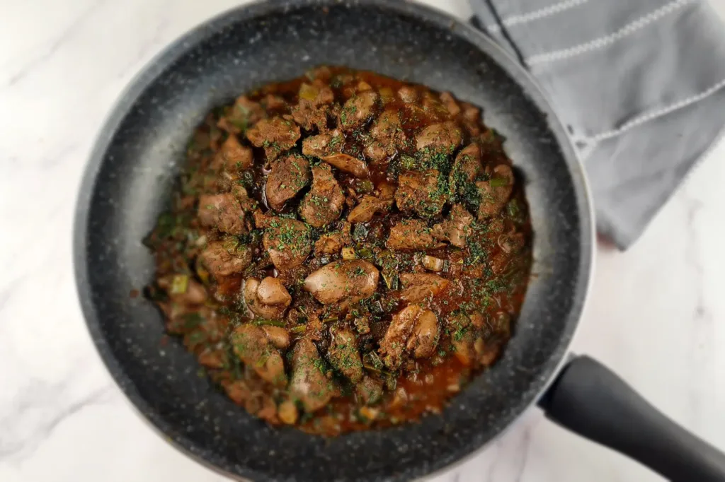 A sizzling pan of keto chicken liver mixed with herbs, cooked to perfection and ready to be served with cauliflower mash.