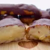 A close-up image of Keto Chocolate Eclairs displayed on a wooden surface. One eclair is cut in half, exposing the creamy filling inside, while others remain whole with a glossy chocolate coating.