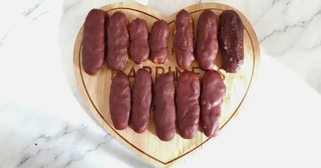 A collection of Keto Chocolate Eclairs neatly arranged on a heart-shaped wooden board, set against a white marble background.