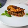 A keto-friendly dish of Mediterranean infused chicken fillets, served on a white plate with keto Mediterranean rice, garnished with basil and red pepper.