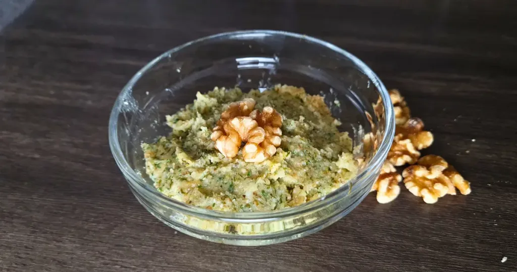 A bowl of walnut pesto garnished with whole walnuts on a wooden surface.