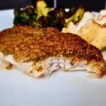 A close-up image of a keto Mediterranean cod with a walnut crust, served with roasted vegetables and walnuts on a white plate.