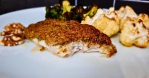 A close-up image of a keto Mediterranean cod with a walnut crust, served with roasted vegetables and walnuts on a white plate.