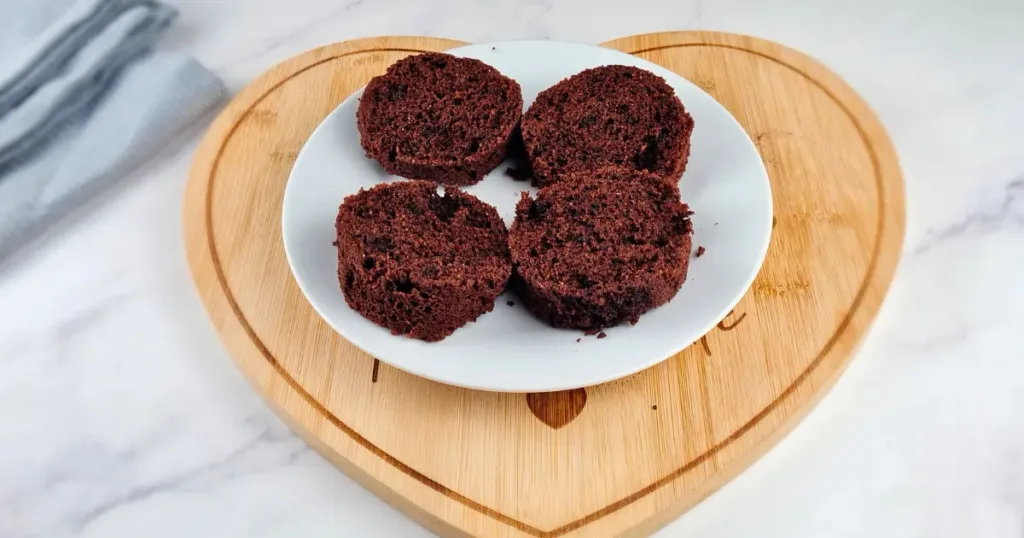 Four slices of a rich, moist Keto Oreo Mug Cake displayed on a white plate, which is placed on a round wooden board, set against a marble countertop with a grey cloth in the background.