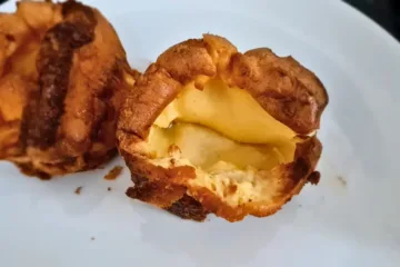 Two keto Yorkshire puddings on a white plate. The puddings are golden brown in color and have a crispy texture. The plate is white and has a red rim.