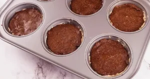 Six chocolate bases for keto peanut butter ice cream sandwiches in a muffin tin.