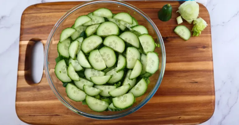 Sliced cucumbers, lettuce, and onions on a cutting board next to a bowl of keto egg salad dressing.