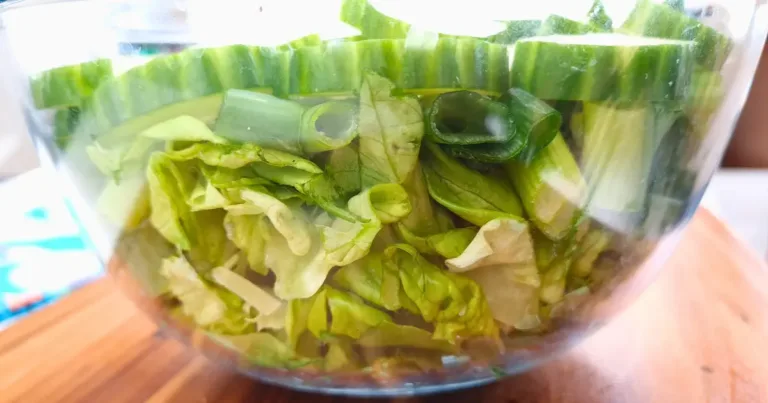 A clear mixing bowl filled with freshly chopped green vegetables including lettuce and spring onions, in preparation for making keto egg salad.