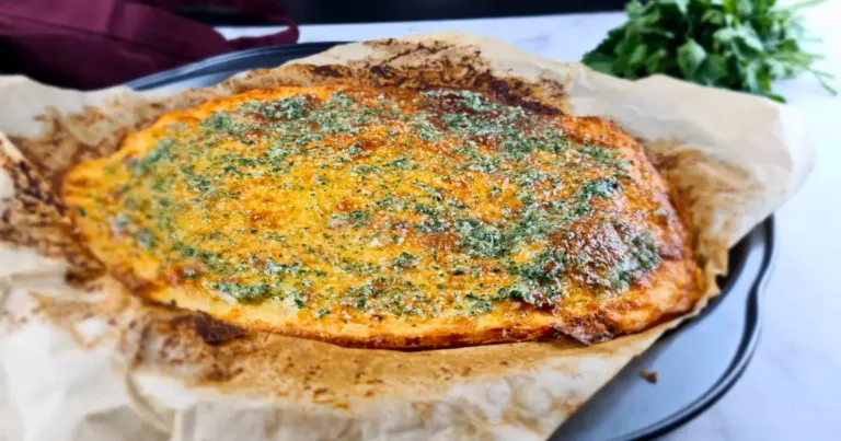 A golden brown keto garlic bread topped with herbs, resting on a piece of parchment paper.