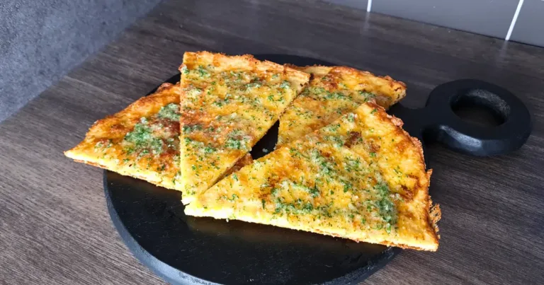 Four slices of golden brown Keto Garlic Bread garnished with herbs, displayed on a black round serving board.