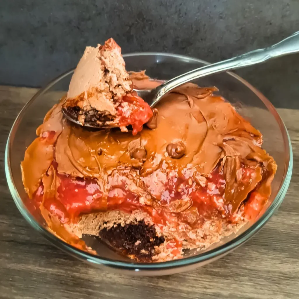 A Keto Mug Cheesecake with chocolate and strawberry jam, fresh strawberries, and chocolate chips on a marble surface.