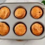 A top view of six golden brown Yorkshire puddings made with almond flour, sitting in a grey baking tray, showcasing a gluten-free option for this classic dish.