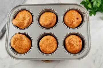 A top view of six golden brown Yorkshire puddings made with almond flour, sitting in a grey baking tray, showcasing a gluten-free option for this classic dish.