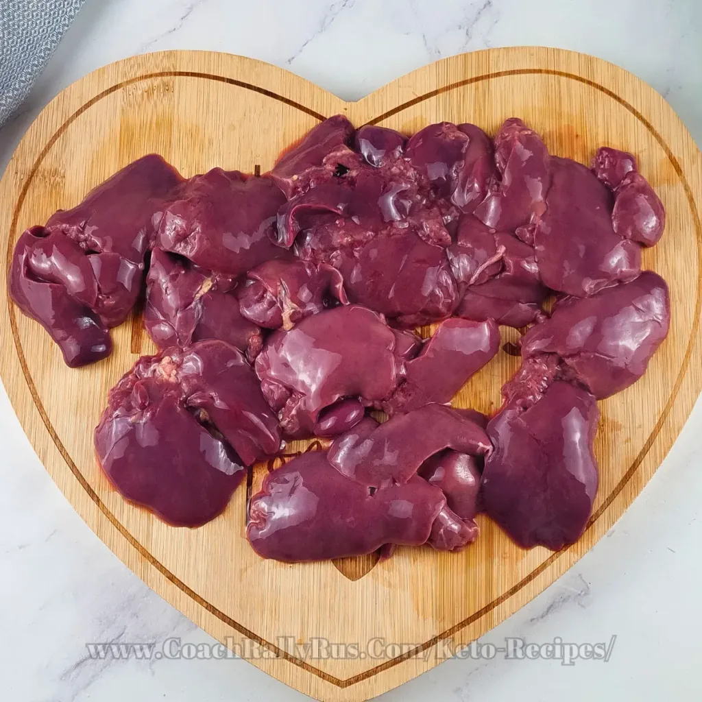 Chicken livers on a wooden board shaped like a heart, showing their dark brown hue and smooth surface.