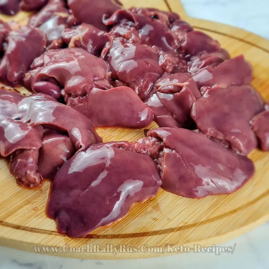 Chicken livers on a wooden board shaped like a heart, showing their dark brown hue and smooth surface.