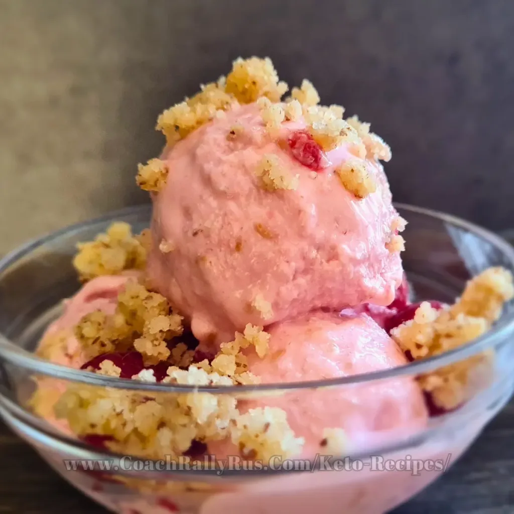 A delectable serving of raspberry cottage cheese ice cream, garnished with crumbled keto-friendly toppings, presented in a clear bowl against a muted background, showcasing a high-protein and low-carb dessert option.