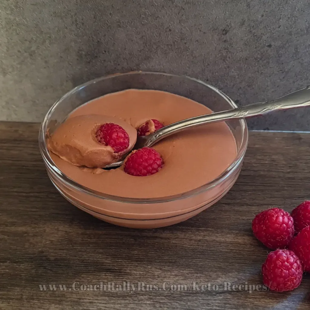 Rich and creamy whipped cottage cheese chocolate mousse topped with fresh raspberries, served in an elegant glass bowl, perfect for a keto-friendly dessert.