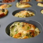 A tray of freshly baked cottage cheese egg muffins with pancetta, showing the golden-brown tops and visible bits of green herbs.