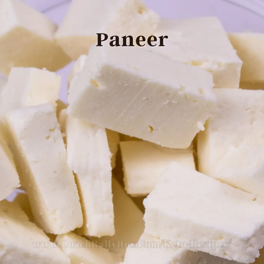 Freshly cut paneer cubes piled on a plate, with the word ‘Paneer’ overlaid at the top and a partially visible website URL at the bottom, suggesting a keto recipe context