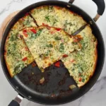 Golden-brown Keto Cottage Cheese Frittata with Pancetta and Broccoli in a black skillet, served on a white marble countertop beside a pink cloth.