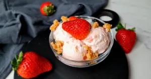 A delectable serving of Keto Strawberry Cottage Cheese Ice Cream, garnished with a fresh strawberry and crumbly topping, presented in an elegant bowl, perfect for a low-carb dessert option.