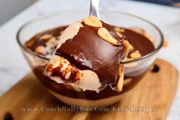 Indulgent Keto Snickers Mousse with layers of smooth cottage cheese and peanut butter blend, topped with a rich chocolate sauce and garnished with whole peanuts, served in a clear glass bowl with a spoonful being lifted, highlighting the dessert’s creamy consistency