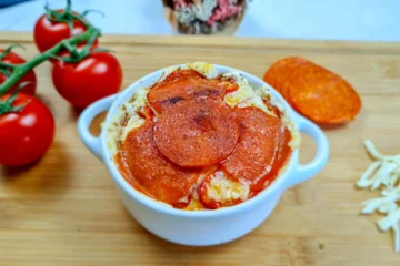 Delicious keto-friendly Cottage Cheese Pizza Bowl topped with savory pepperoni slices, garnished with fresh herbs, and served in a white bowl on a rustic wooden table, ready to enjoy.