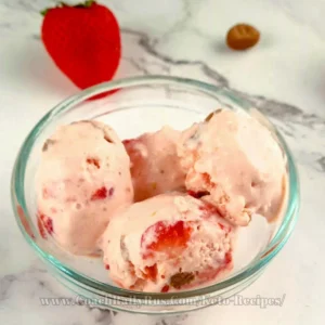 A sumptuous scoop of keto strawberry cheesecake ice cream, garnished with fresh strawberry pieces and crumbled cheesecake crust, served in a stylish glass bowl on a chic marble countertop, embodying a perfect blend of health-conscious indulgence and gourmet dessert presentation.