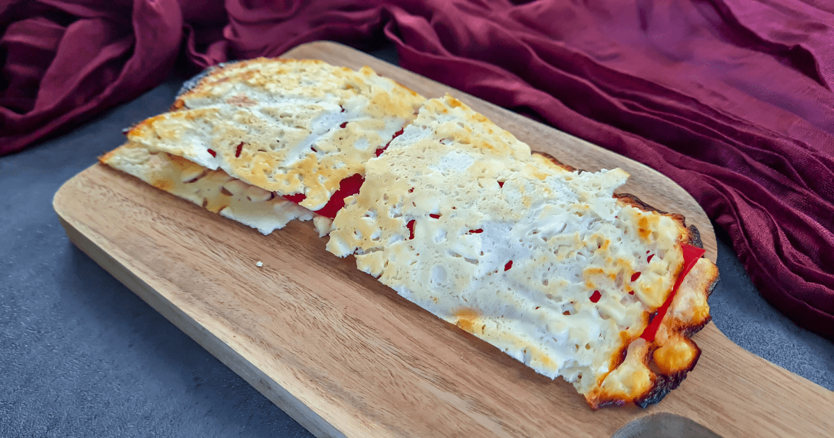 A golden-brown cottage cheese flatbread, freshly baked and full of texture with small, white lumps of cottage cheese visible, sits on parchment paper inside a baking tray, showcasing its homemade, high-protein, and low-carb qualities.