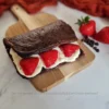 A scrumptious 4-Ingredient Chocolate Cottage Cheese Flatbread, beautifully presented on a wooden board, with a layer of creamy cottage cheese and fresh strawberry slices on top, inviting you to take a bite. The backdrop features a hint of a red cloth and a sprinkle of chocolate chips, adding to the homemade charm of this delightful keto dessert.