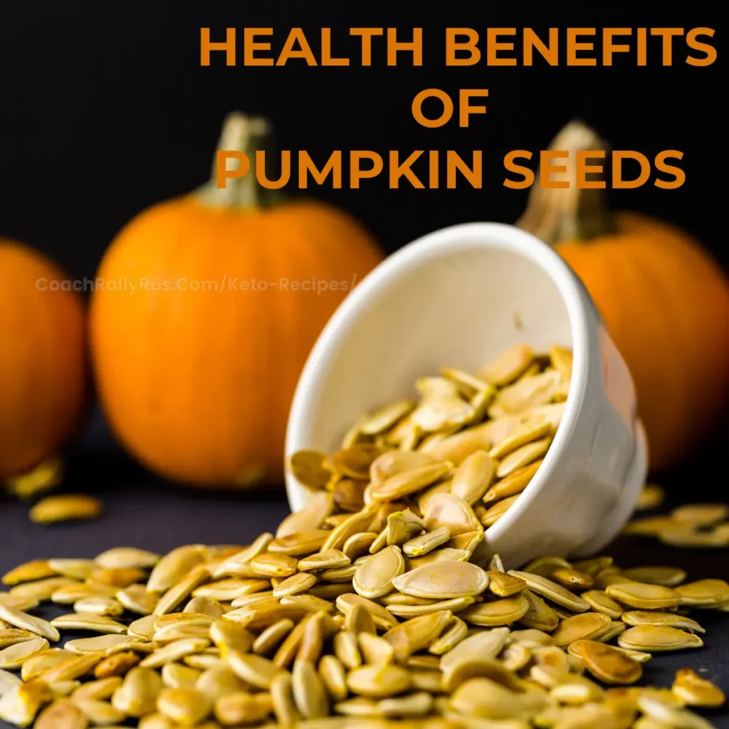 A white bowl tipped over, spilling pumpkin seeds onto a dark surface with whole pumpkins in the background. Text overlay states ‘HEALTH BENEFITS OF PUMPKIN SEEDS’ with a website address ‘CoachRallyRus.com/Keto-Recipes’ below.