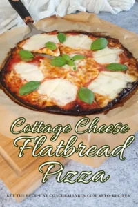 A freshly baked Cottage Cheese Flatbread Pizza Margherita with a golden-brown crust, topped with melted mozzarella cheese, vibrant red tomato sauce, and fresh green basil leaves. The pizza is presented on parchment paper with a pizza cutter alongside. Text overlay states ‘Cottage Cheese Flatbread Pizza’ and prompts to get the recipe at a website link.