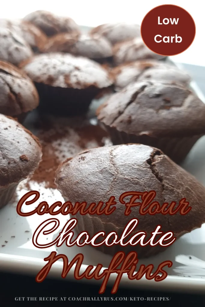 A close-up image of freshly baked coconut flour chocolate muffins with a light dusting of cocoa powder on top, arranged on a white plate against a bright background.