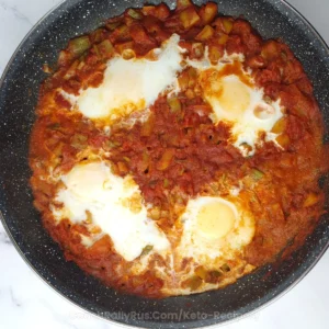 A close-up image of a keto shakshuka in a skillet, featuring poached eggs nestled in a bed of chunky tomato sauce with diced vegetables, cooked to perfection.