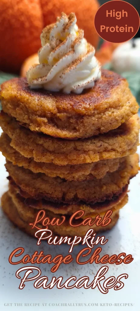 A stack of golden-brown Keto Pumpkin Spice Cottage Cheese Protein Pancakes topped with a dollop of cream, garnished with a sprinkle of spice. In the background, there’s a blurred image of pumpkins.