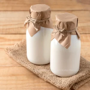 Two glass bottles of kefir with rustic paper covers, set on a burlap cloth over a wooden background.