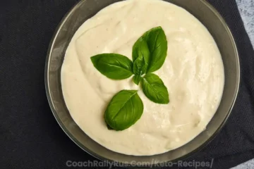 A bowl of creamy Keto Cottage Cheese Alfredo Sauce on a dark napkin with the website “CoachRallyRus.com/Keto-Recipes” at the bottom.