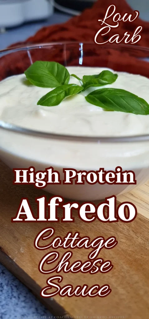 A glass bowl filled with creamy Alfredo Cottage Cheese Sauce, garnished with fresh basil leaves on top, set against a kitchen counter backdrop.
