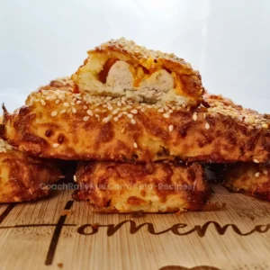 Golden-brown keto sausage rolls topped with sesame seeds on a wooden cutting board.